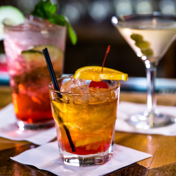 Three cocktails on a bar, including an Old Fashioned, a pink drink, and a martini.