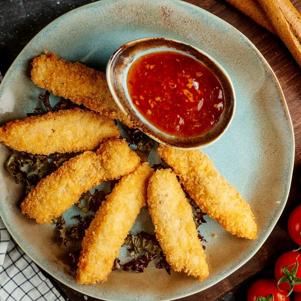 Crispy golden-brown chicken tenders with a side of sweet chili dipping sauce on a blue plate.