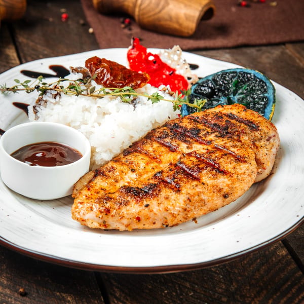 Grilled chicken breast with rice, barbecue sauce, sun-dried tomatoes, and a charred lime.