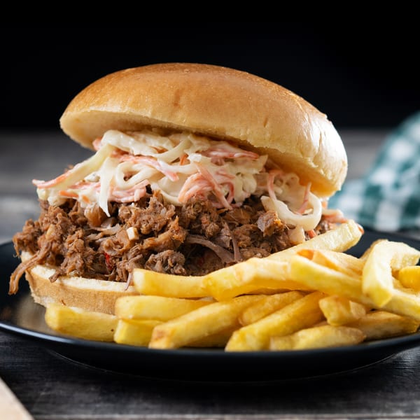 Pulled pork sandwich with coleslaw and a side of golden fries on a black plate.