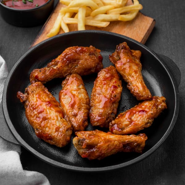 Seven glazed chicken wings in a black skillet, with fries and ketchup in the background.