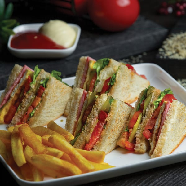 Club sandwiches with ham, cheese, lettuce, tomato, and pickles, served with french fries.