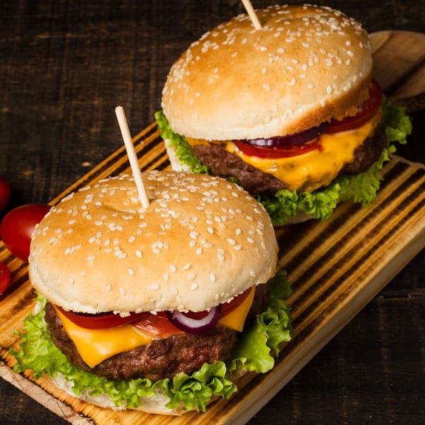 Two Wild Duck Bar & Grill cheeseburgers with lettuce, tomato, and onion on a wooden board.